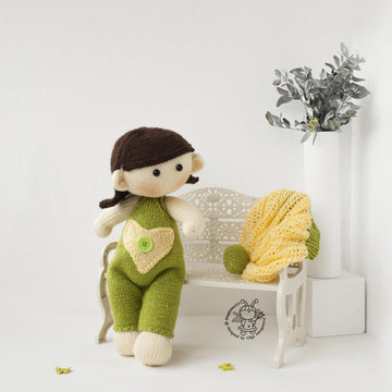 Baby doll in green overalls knitting flat