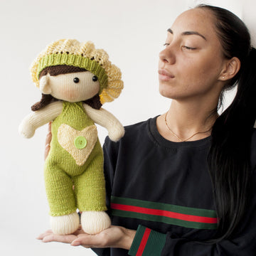 Baby doll in green overalls knitting flat