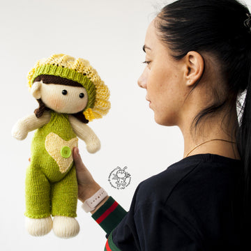 Baby doll in green overalls knitting flat