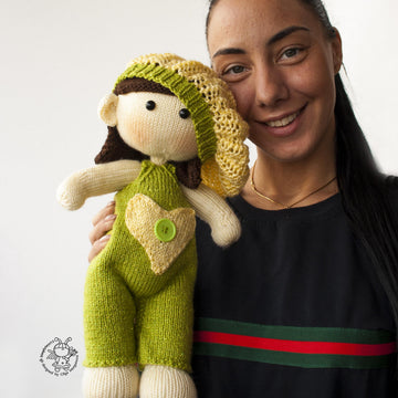 Baby doll in green overalls knitting flat